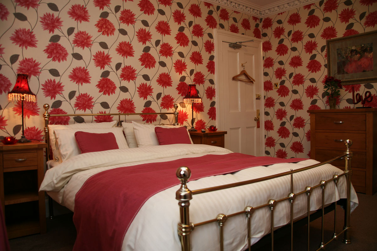 Large double bed with red floral wallpaper